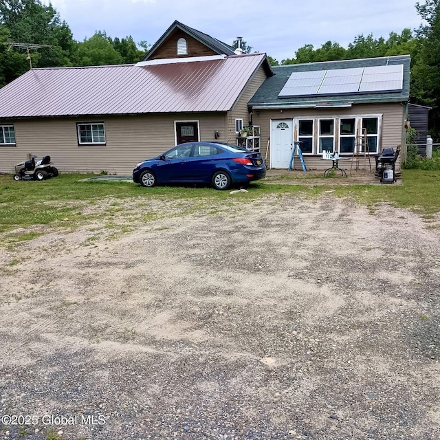 view of front of home featuring metal roof, roof mounted solar panels, and driveway