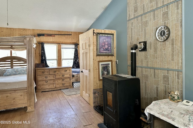 bedroom with wood walls, lofted ceiling, a wood stove, hardwood / wood-style flooring, and a textured ceiling