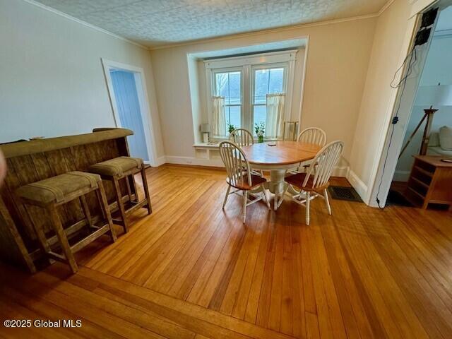 dining room featuring visible vents, baseboards, light wood-style flooring, ornamental molding, and a textured ceiling