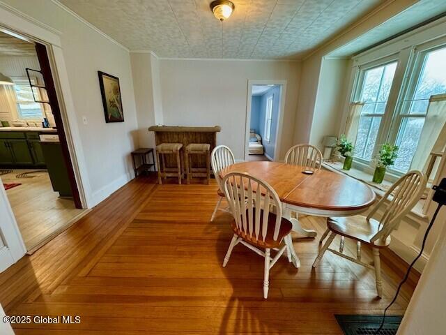 dining space with baseboards, ornamental molding, and light wood-style flooring