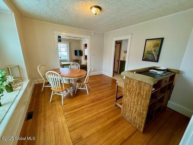 dining room featuring a textured ceiling, wood finished floors, visible vents, baseboards, and crown molding