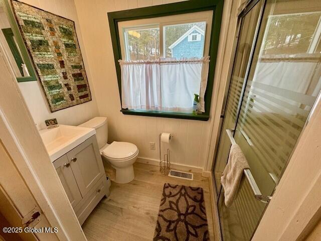 bathroom with toilet, wood finished floors, a shower stall, and visible vents