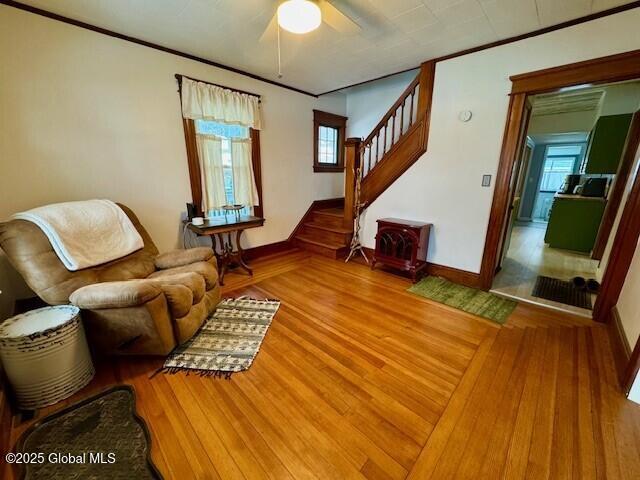 living area with stairs, baseboards, wood finished floors, and crown molding