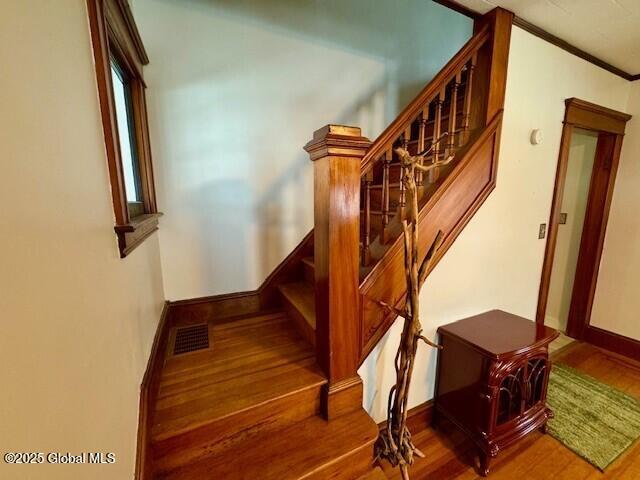 stairs featuring visible vents, crown molding, baseboards, and wood finished floors