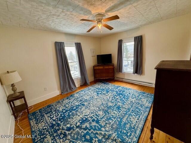 bedroom featuring multiple windows, hardwood / wood-style floors, baseboard heating, and baseboards