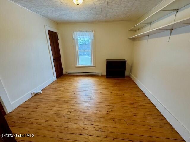 spare room with light wood finished floors, baseboard heating, and baseboards