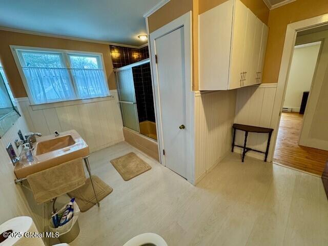 full bath featuring ornamental molding, wainscoting, a shower with door, and wood finished floors