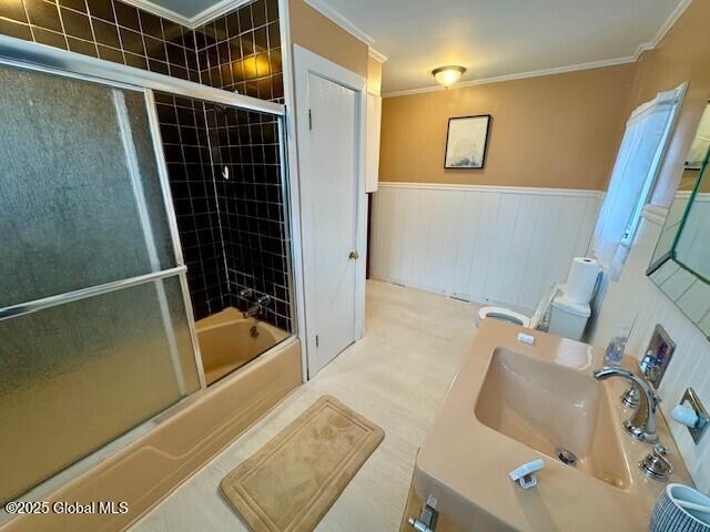 full bath featuring combined bath / shower with glass door, wainscoting, a sink, and crown molding