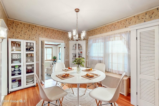 dining room featuring light wood finished floors, ornamental molding, a notable chandelier, and wallpapered walls