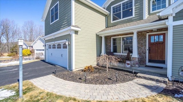 view of home's exterior featuring a shingled roof, stone siding, aphalt driveway, an attached garage, and covered porch