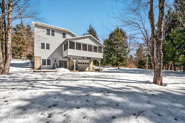 snow covered back of property featuring a garage and a sunroom