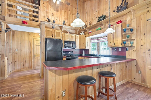 kitchen with wooden walls, a peninsula, light wood-style flooring, black appliances, and dark countertops