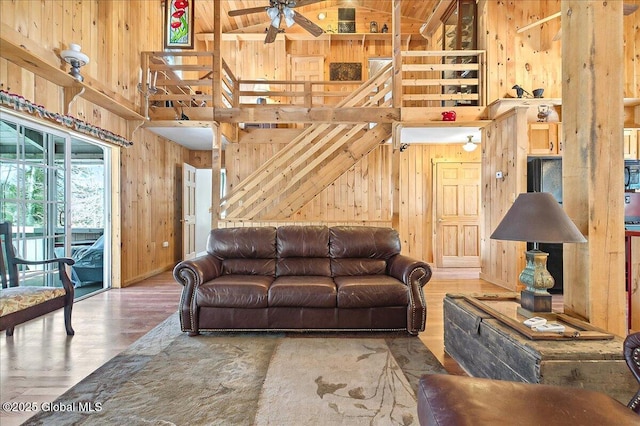 living area featuring ceiling fan, wood finished floors, wood walls, and a towering ceiling