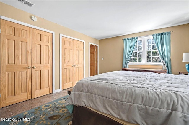 bedroom with tile patterned floors, visible vents, and two closets