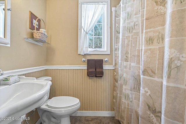 full bathroom with toilet, a wainscoted wall, wood walls, and a sink