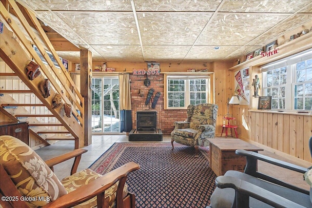 living room featuring stairway, wood walls, a wood stove, and tile patterned flooring