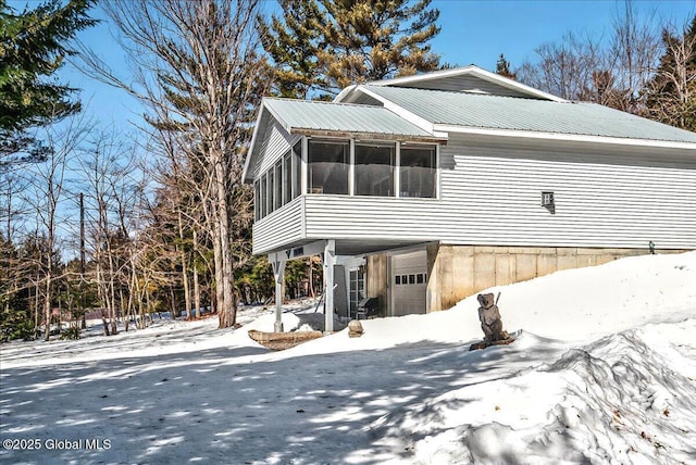 view of snow covered exterior with a carport, metal roof, a garage, and a sunroom