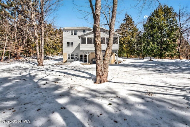 snow covered back of property featuring a sunroom