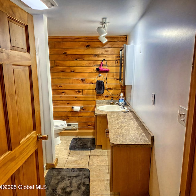 half bathroom featuring tile patterned flooring, vanity, toilet, and wooden walls