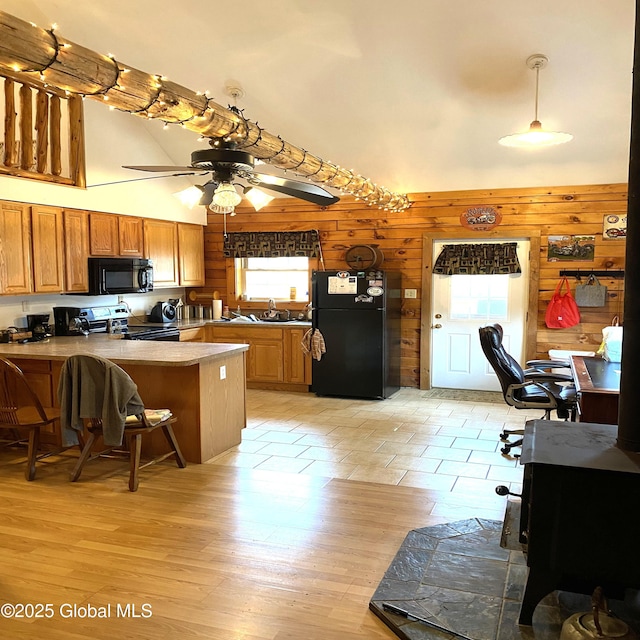 kitchen featuring brown cabinetry, ceiling fan, a peninsula, wood walls, and black appliances