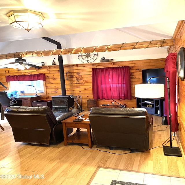 living room featuring ceiling fan, a wood stove, wood walls, and wood finished floors