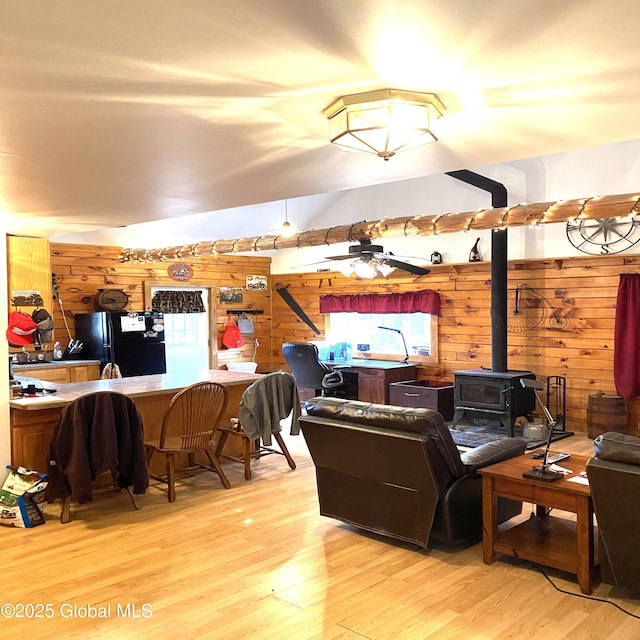 living room featuring ceiling fan, wood finished floors, a wood stove, vaulted ceiling, and wood walls