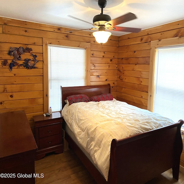 bedroom with wooden walls, a ceiling fan, and wood finished floors