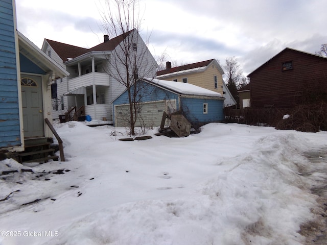 view of snow covered exterior featuring entry steps, a detached garage, a balcony, and a chimney