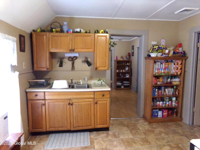 kitchen featuring visible vents, brown cabinets, a sink, light countertops, and vaulted ceiling