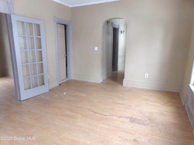 empty room featuring baseboards, wood finished floors, arched walkways, and ornamental molding