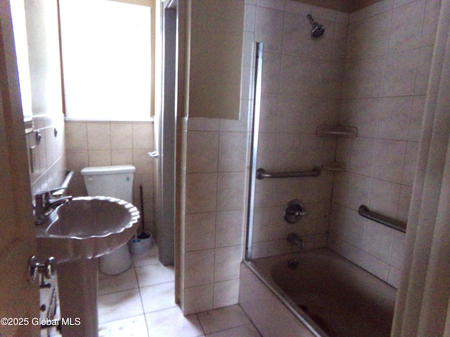 bathroom with toilet, a sink, tiled shower / bath combo, tile walls, and tile patterned flooring