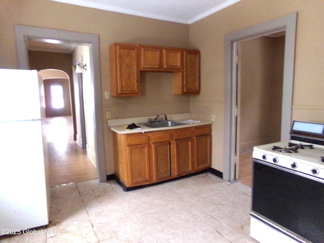 kitchen featuring brown cabinets, a sink, white appliances, arched walkways, and light countertops