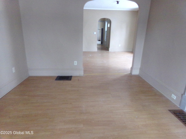 unfurnished room with baseboards, visible vents, arched walkways, and light wood-type flooring