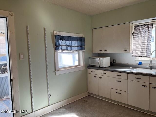 kitchen with white microwave, baseboards, white cabinetry, and a sink