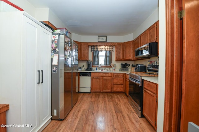 kitchen featuring light wood-style flooring, appliances with stainless steel finishes, brown cabinets, light countertops, and a sink