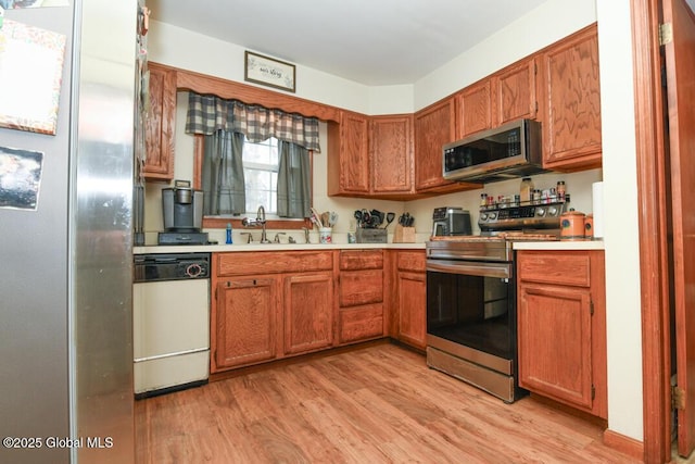 kitchen featuring stainless steel appliances, light wood-style floors, light countertops, and a sink