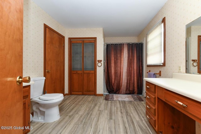 full bathroom featuring toilet, wallpapered walls, wood finished floors, and vanity