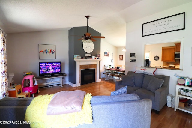 living room with lofted ceiling, ceiling fan, a tiled fireplace, and wood finished floors