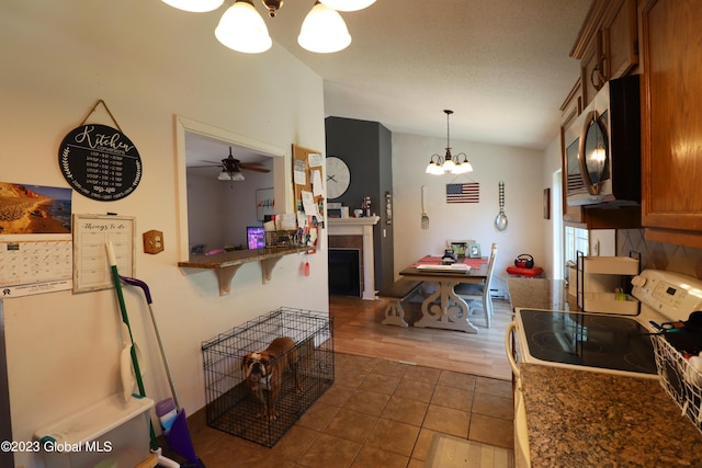 kitchen with brown cabinetry, a tiled fireplace, electric range oven, stainless steel microwave, and vaulted ceiling