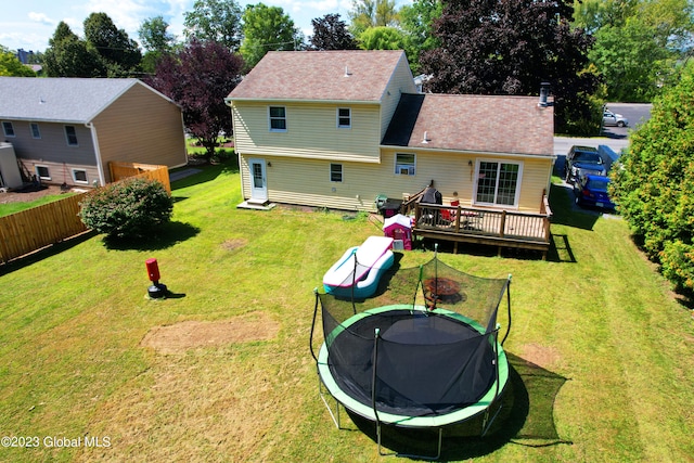 rear view of property with a yard, a trampoline, a wooden deck, and fence