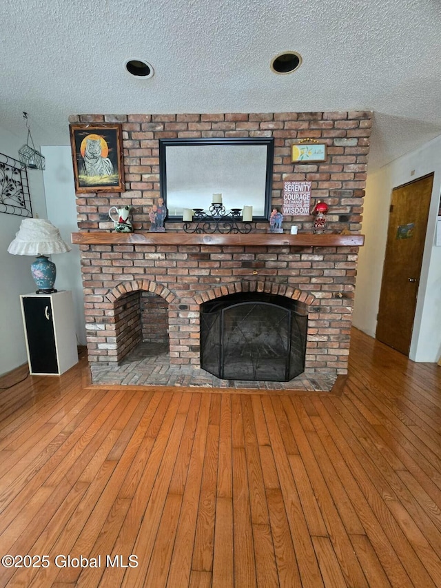 unfurnished living room featuring a brick fireplace, a textured ceiling, and hardwood / wood-style floors