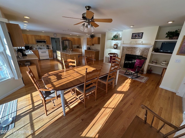 dining room with a ceiling fan, wood finished floors, a fireplace, baseboards, and recessed lighting
