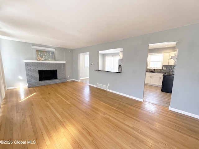 unfurnished living room featuring a brick fireplace, baseboards, visible vents, and light wood-type flooring