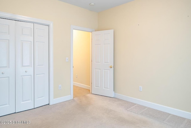 unfurnished bedroom with a closet, light colored carpet, and baseboards