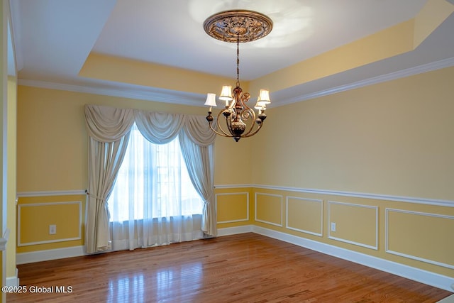 spare room with wood finished floors, an inviting chandelier, a tray ceiling, crown molding, and a decorative wall