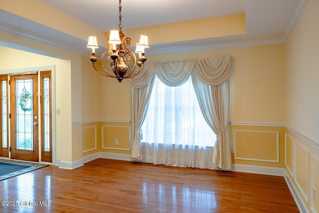 unfurnished room featuring wood finished floors, crown molding, a decorative wall, a raised ceiling, and a chandelier