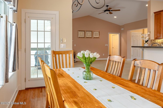 dining room featuring baseboards, light wood-style floors, a ceiling fan, and vaulted ceiling