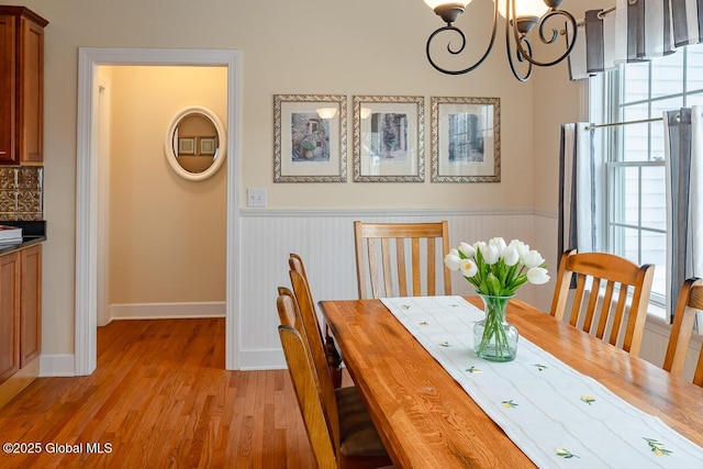 unfurnished dining area with a notable chandelier, a wainscoted wall, and light wood finished floors