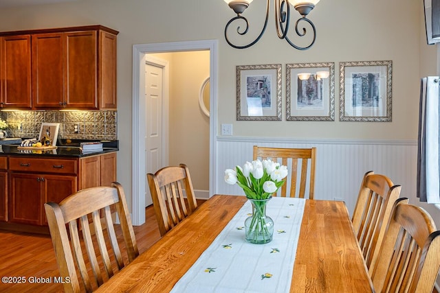 dining room with an inviting chandelier, wood finished floors, and wainscoting