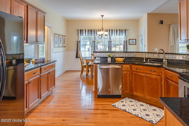 kitchen with light wood finished floors, freestanding refrigerator, a sink, stainless steel dishwasher, and decorative light fixtures